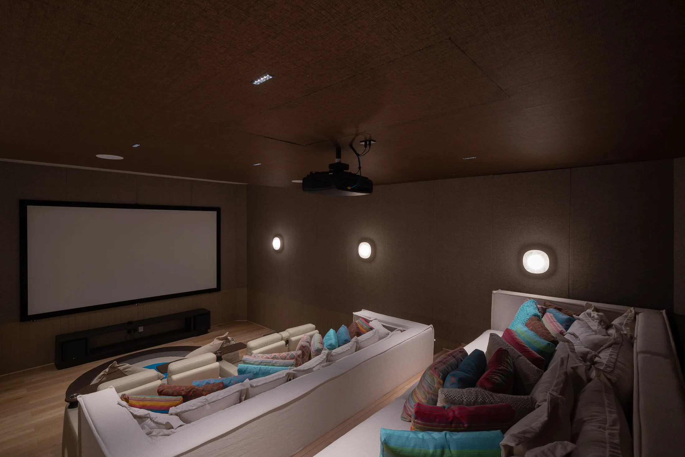 The cinema from the back row — the wide screen, the projector overhead, the sectional heaped with cushions