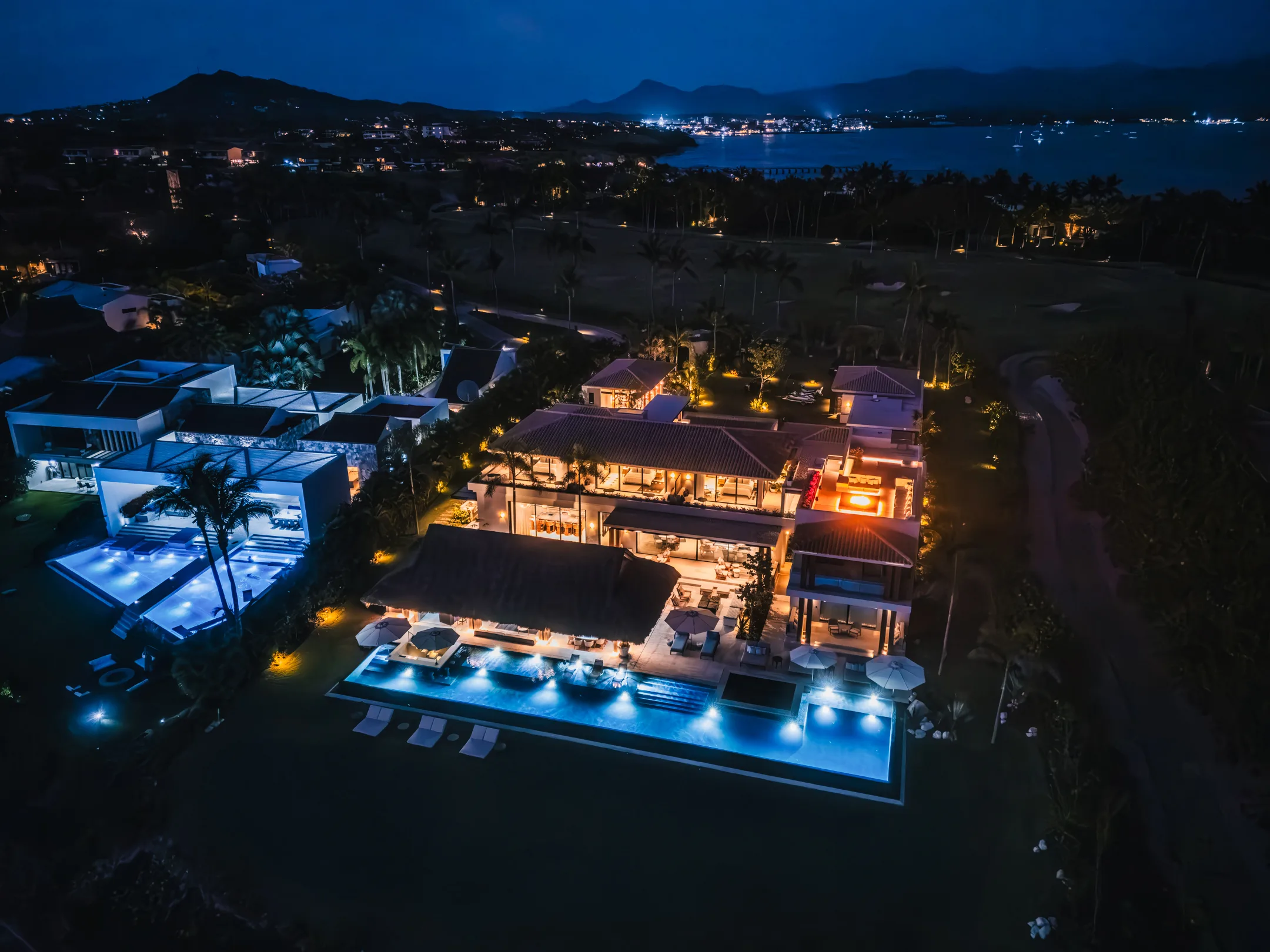A wide night view — the lit estate, the dark fairways, and the lights of Punta Mita across the bay