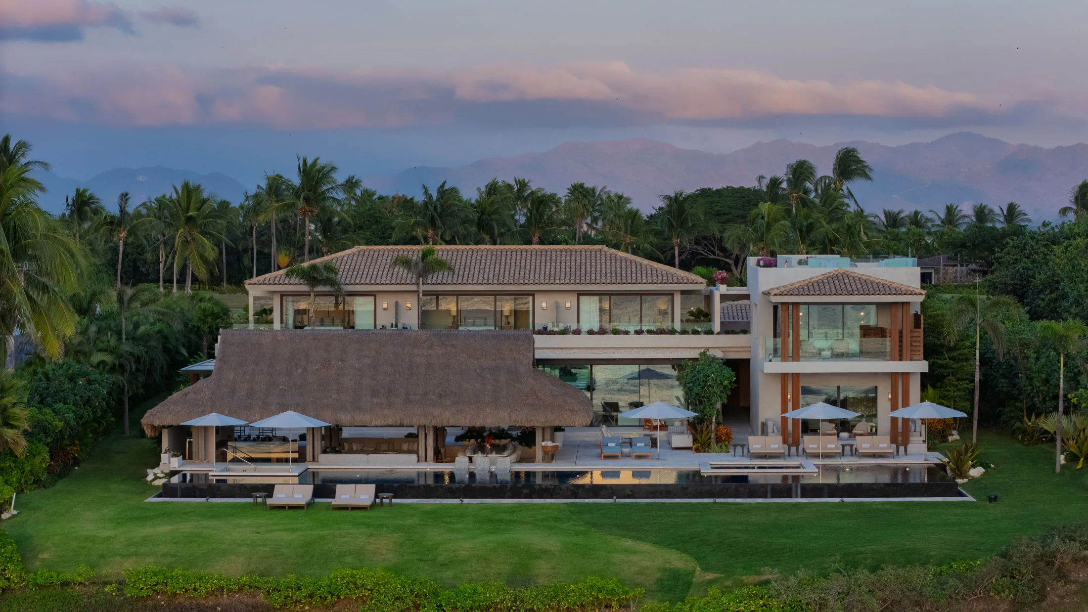 The estate from the garden side under a pink dusk sky, mountains on the horizon