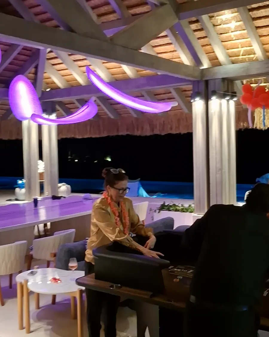 A dealer at the blackjack table under the palapa at night, the lit pool beyond