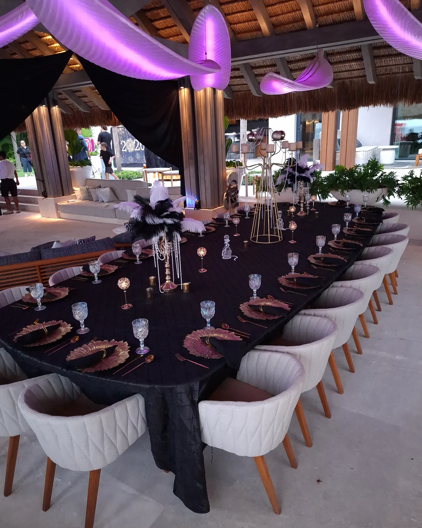 The Gatsby table at dusk — black linens, gold chargers and feather centerpieces under the palapa