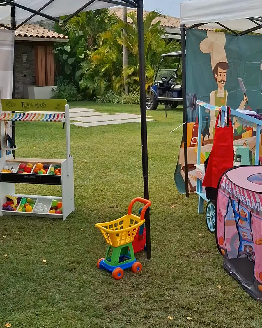 The kids’ market on the lawn — play stalls and a pink ice-cream truck under white canopies