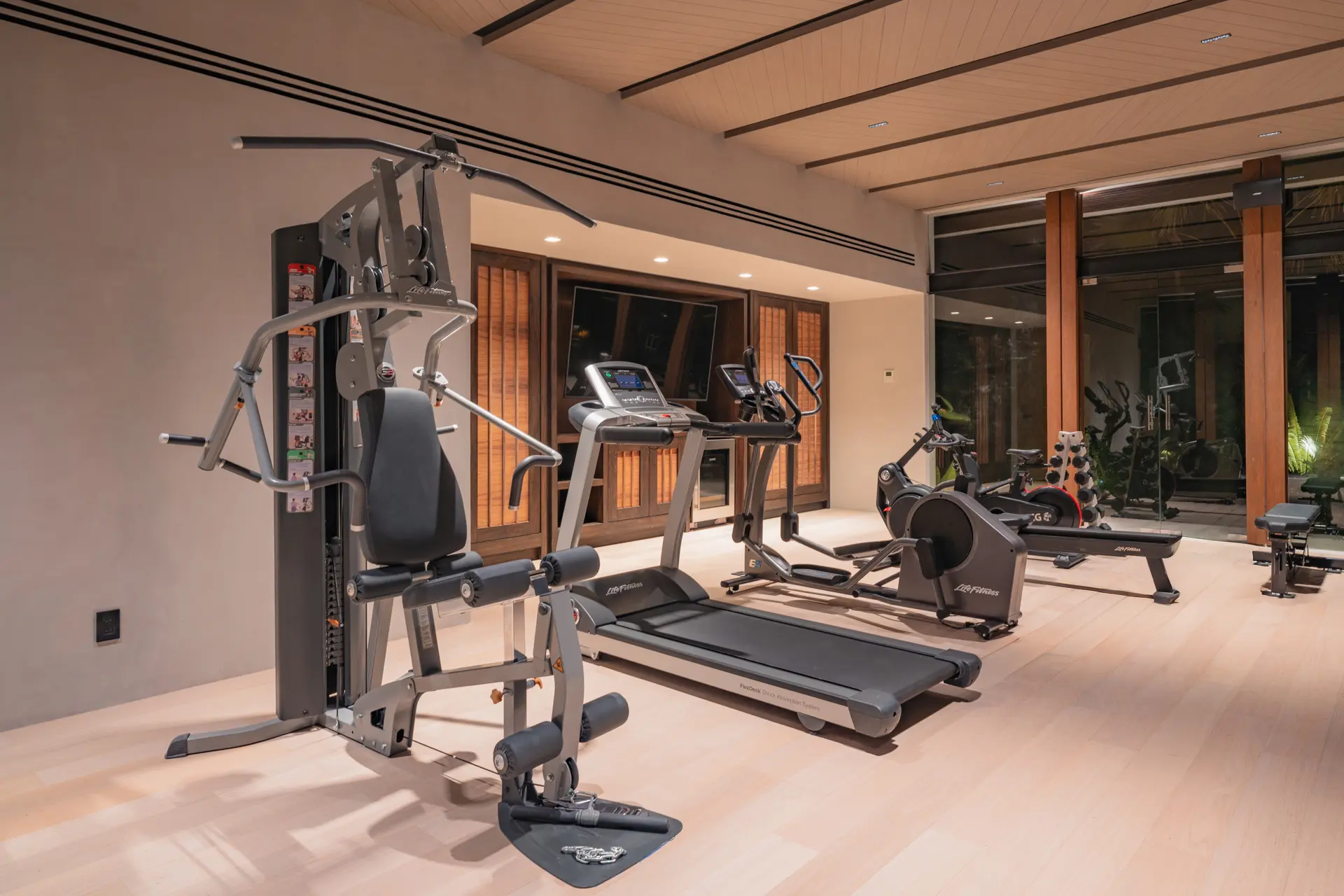 The fitness studio from the cable station — treadmill, elliptical and rower running toward the glass wall