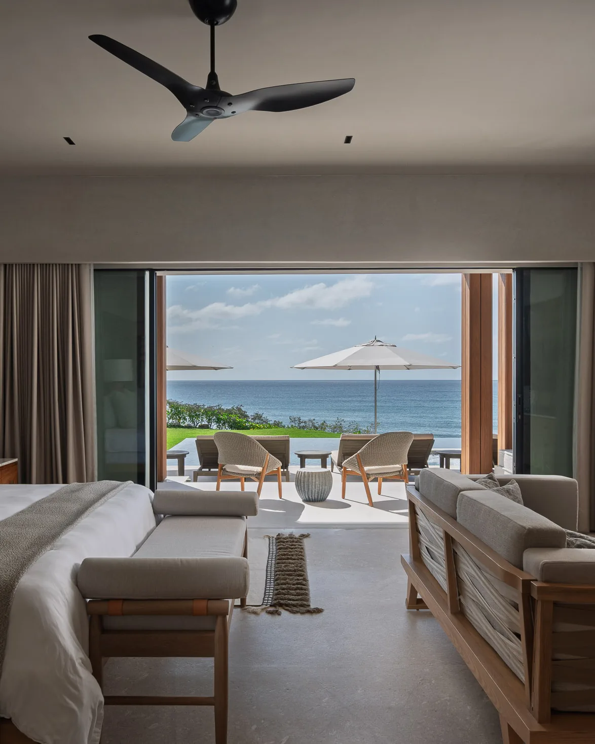 The Ocean Suite — king bed and sitting area open to the terrace, umbrellas and the Pacific beyond