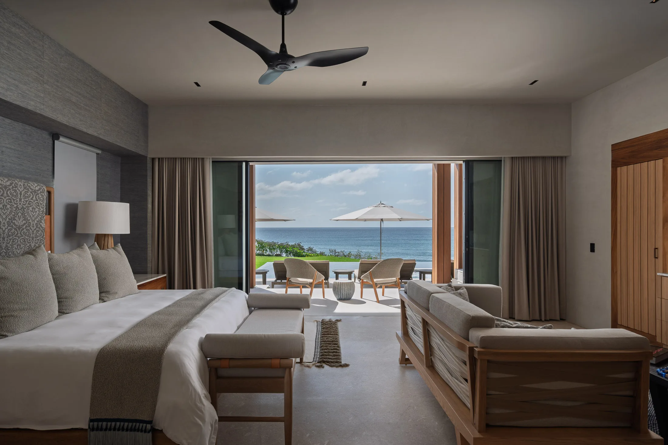 The Ocean Suite — king bed and sitting area open to the terrace, umbrellas and the Pacific beyond