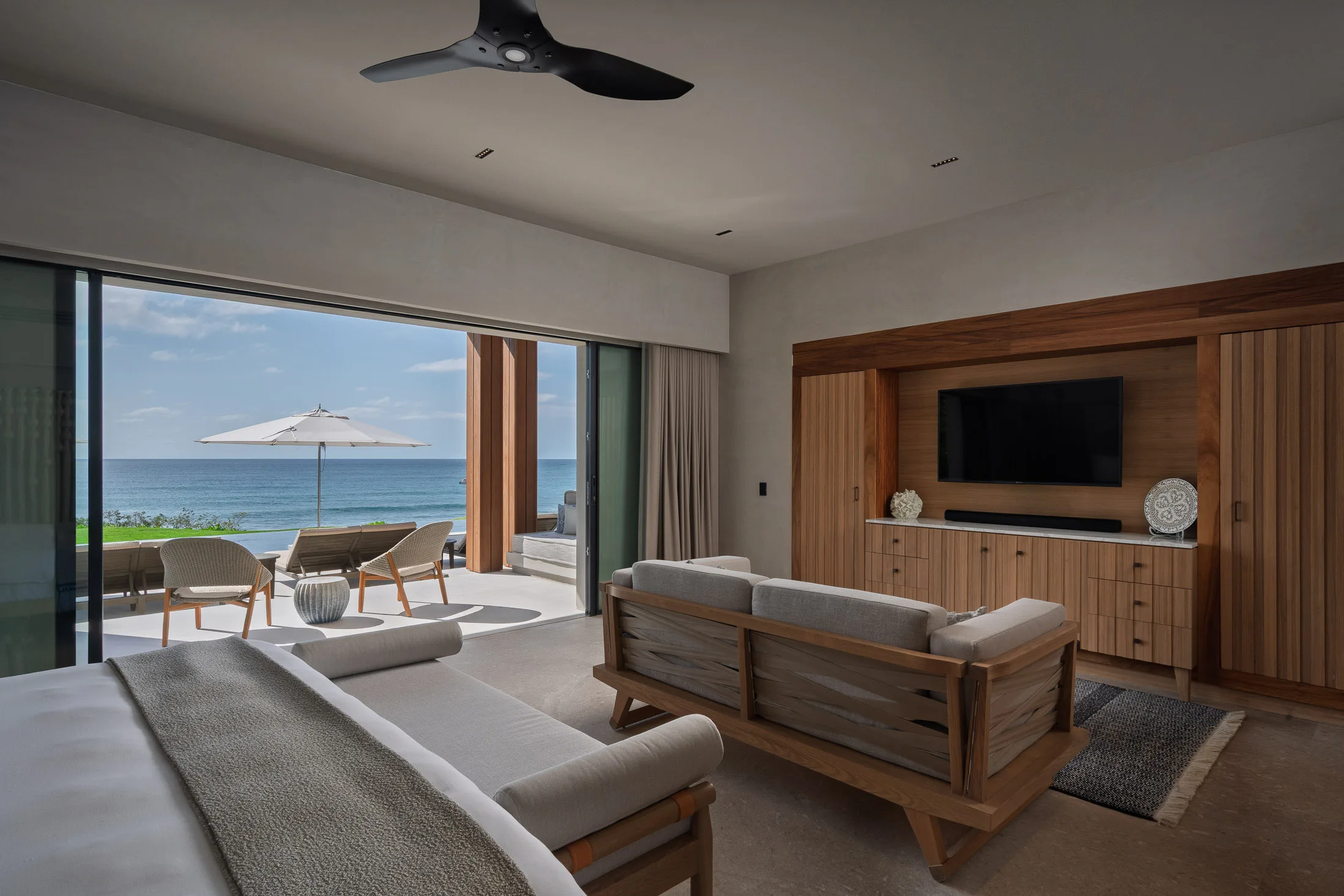 The Ocean Suite’s sitting area — sofa facing the wood-paneled media wall, the ocean terrace beyond
