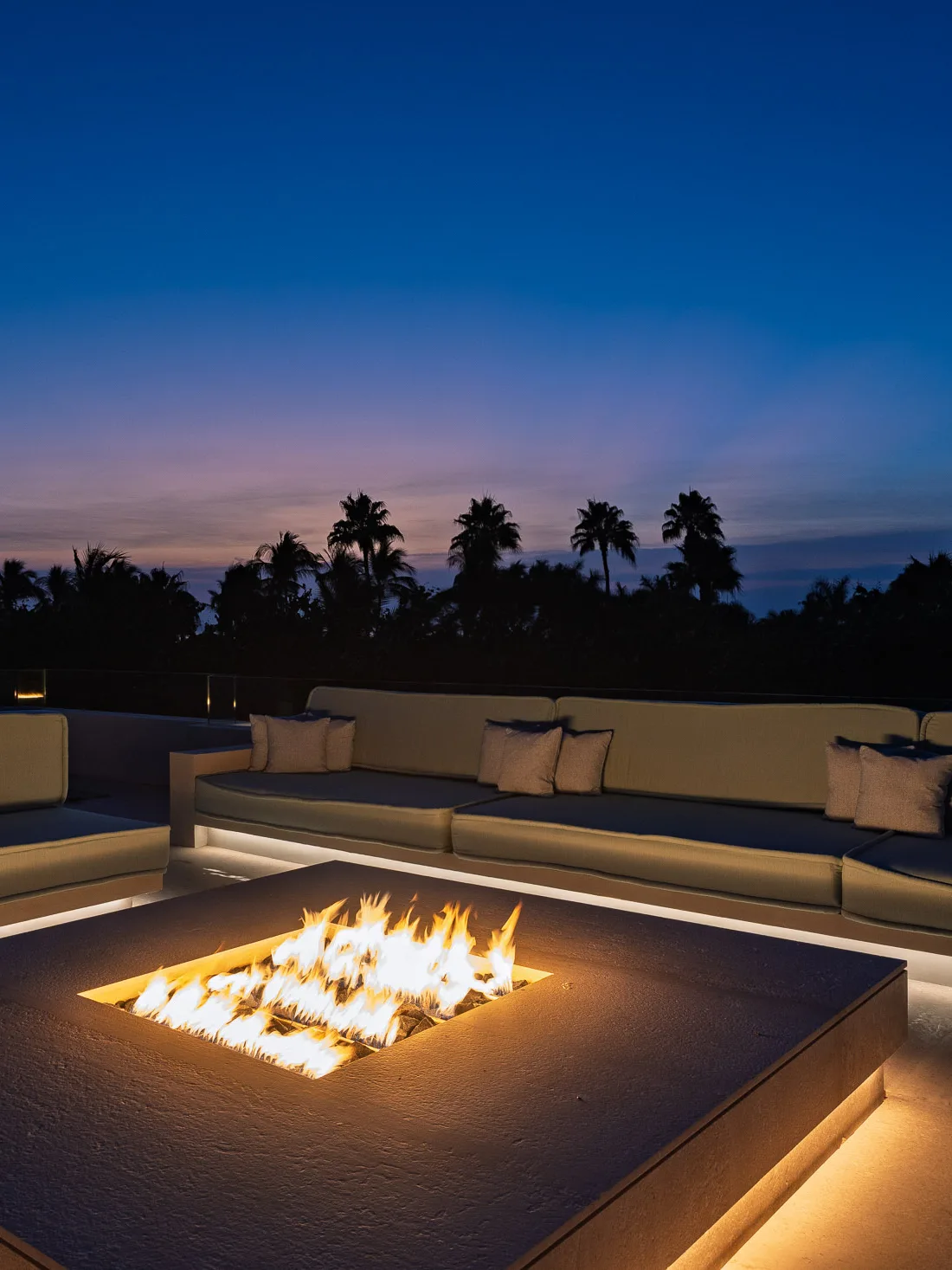 The rooftop at blue hour — the fire table lit, palms in silhouette against the last of the light