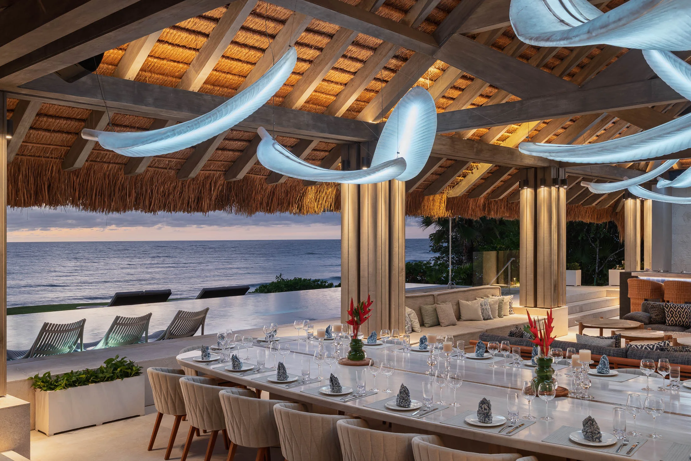 The palapa at sunset — the long table set beneath leaf-shaped lights, the infinity pool and the Pacific beyond