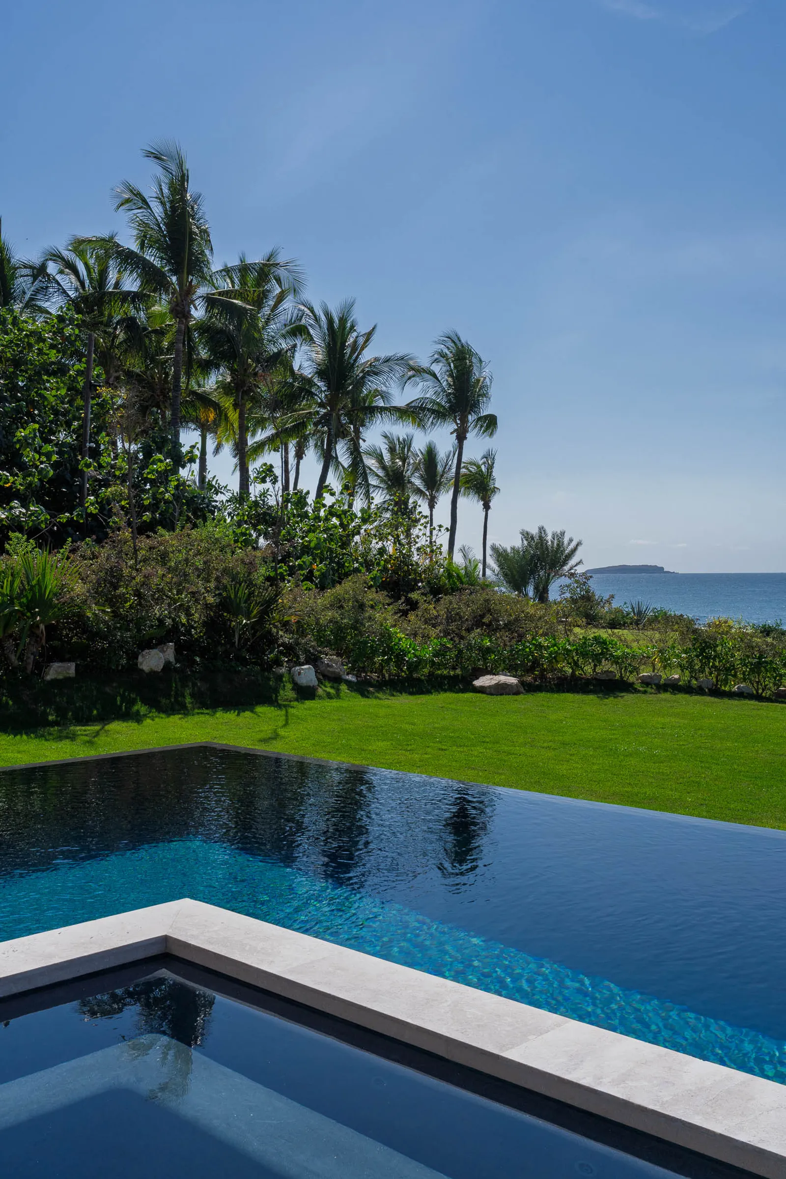 The pool’s corner and hot-tub tier meeting the lawn, palms and the sea beyond