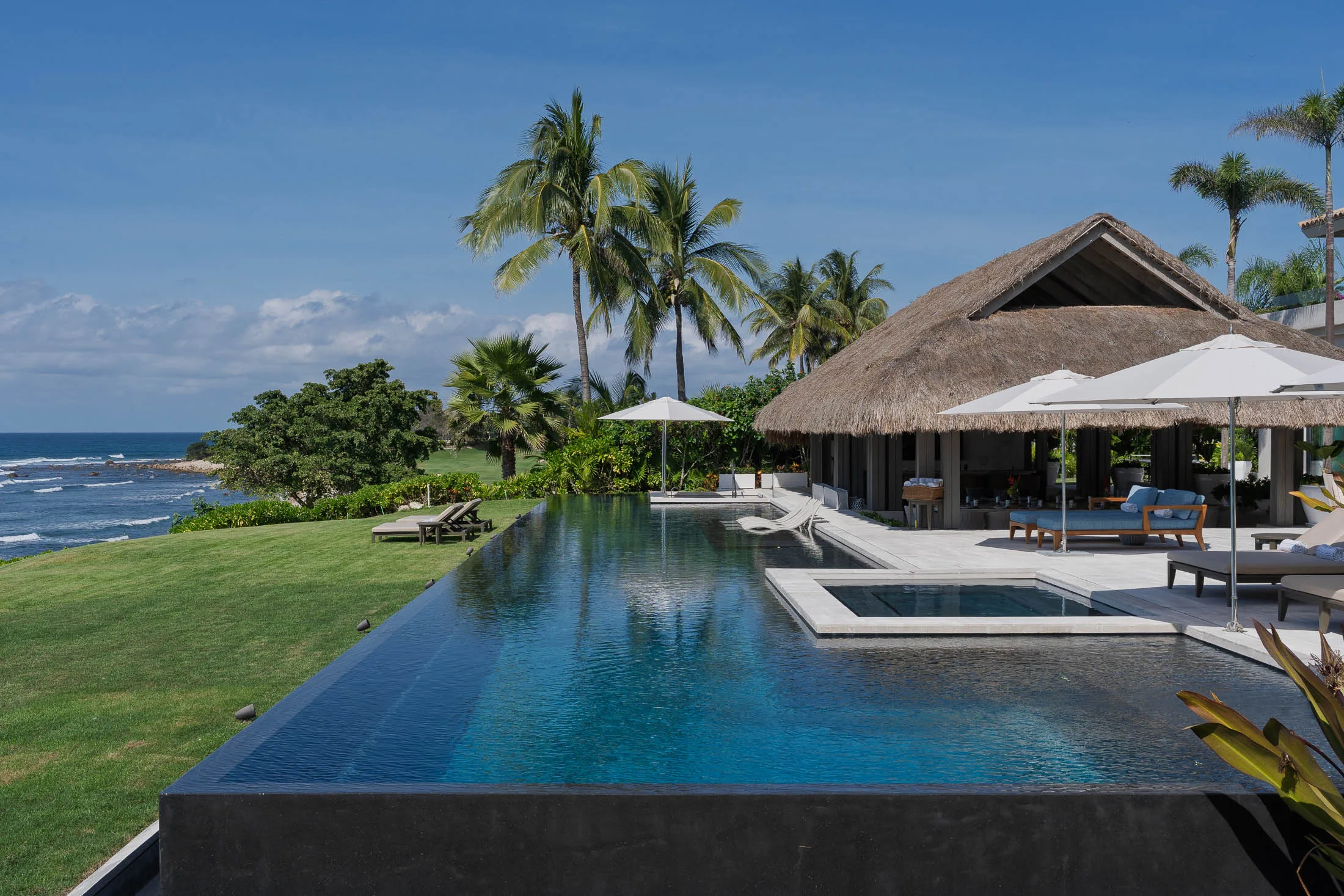 The seventy-foot infinity pool in full sun — its edge running past the palapa to the Pacific