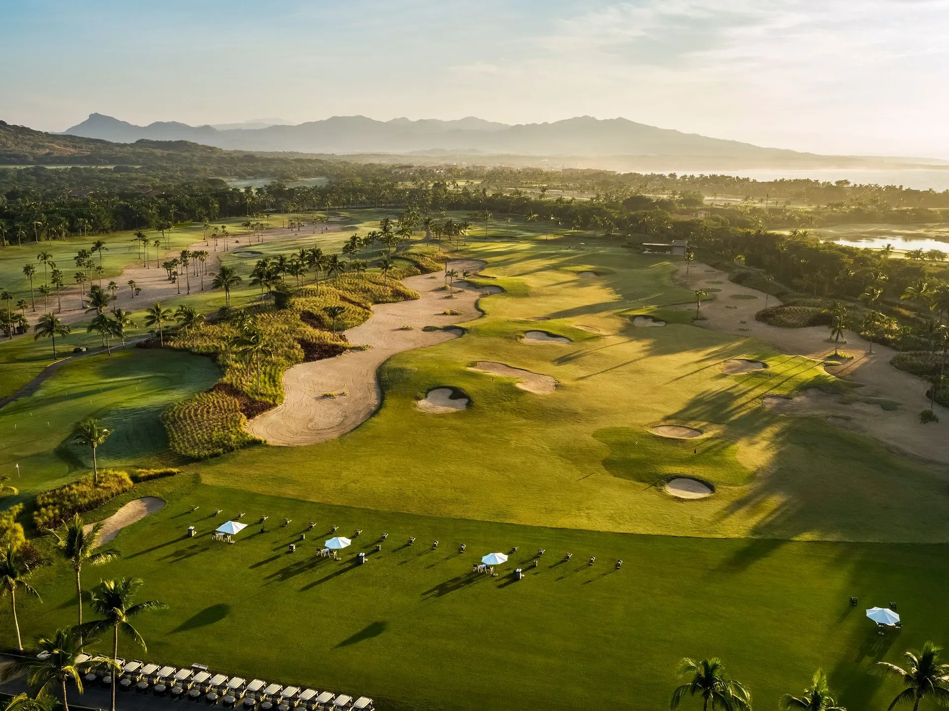 The driving range — golfers under white umbrellas hitting toward the mountains, bunkers and palms across the range