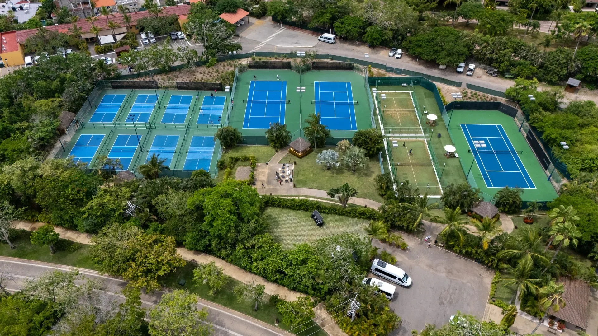 The Racquet Center from above — a block of blue tennis and pickleball courts among the trees