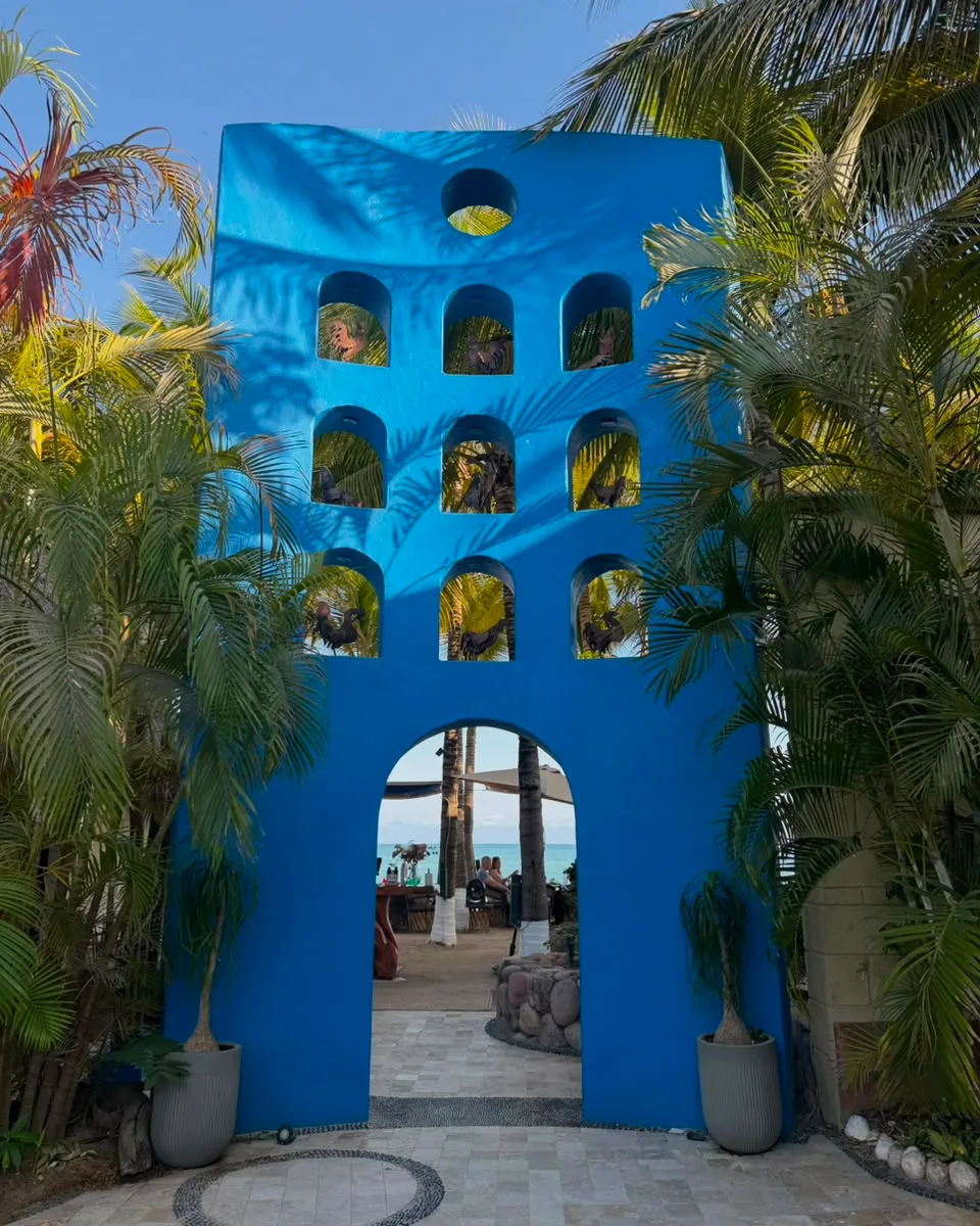 Mina’s cobalt-blue arched entrance tower framed by palms, the beach tables showing through the doorway