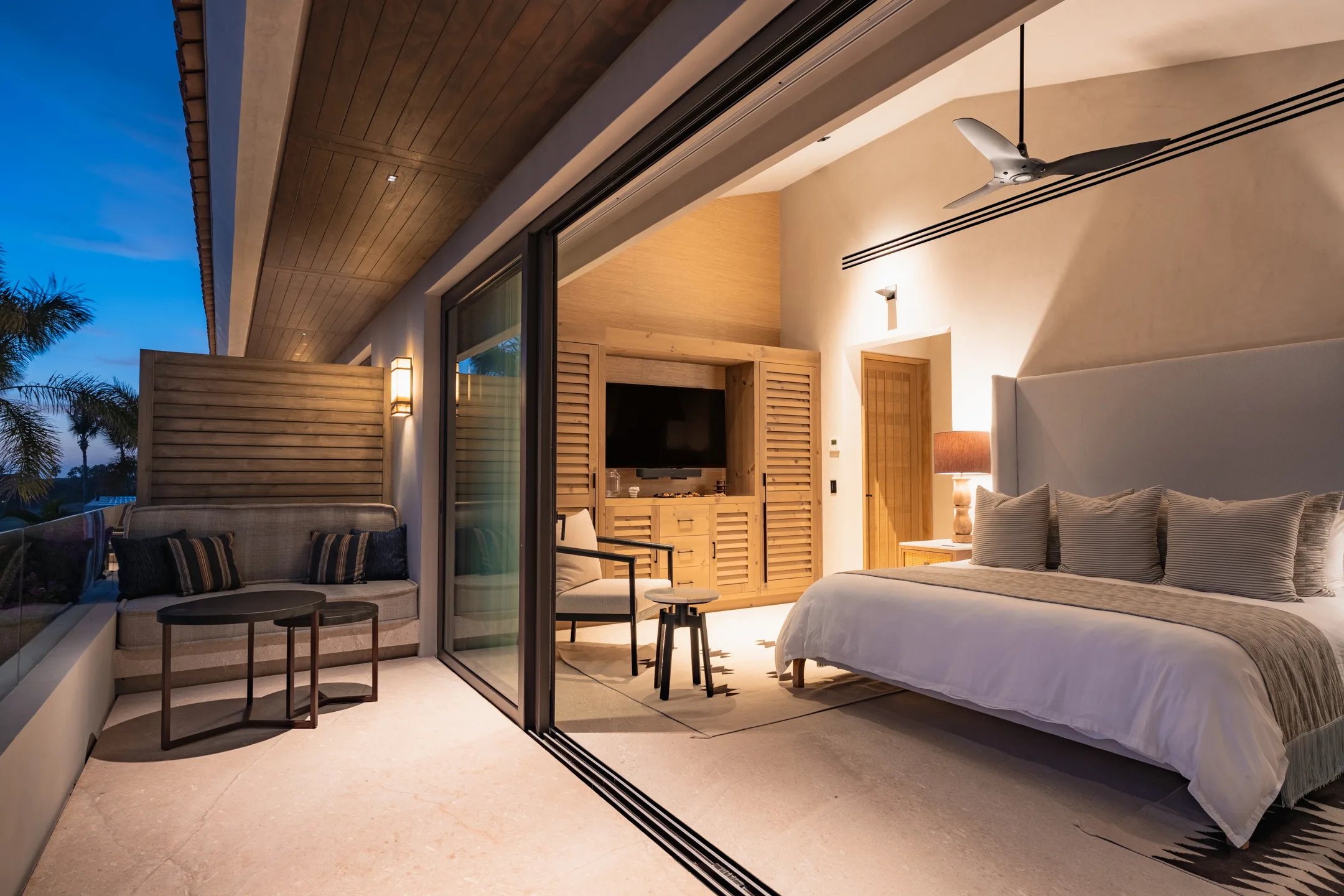 The Rivers Suite from its terrace at golden hour — bed, sitting corner and the television wall glowing warm