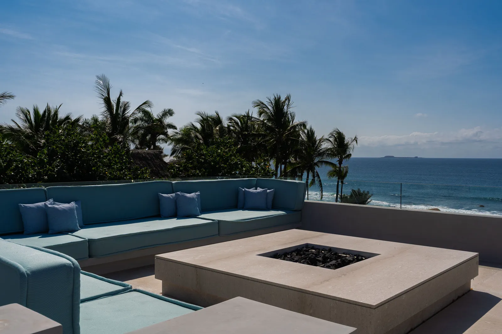 The rooftop lounge by day — sofas around the fire table, the ocean past the palms