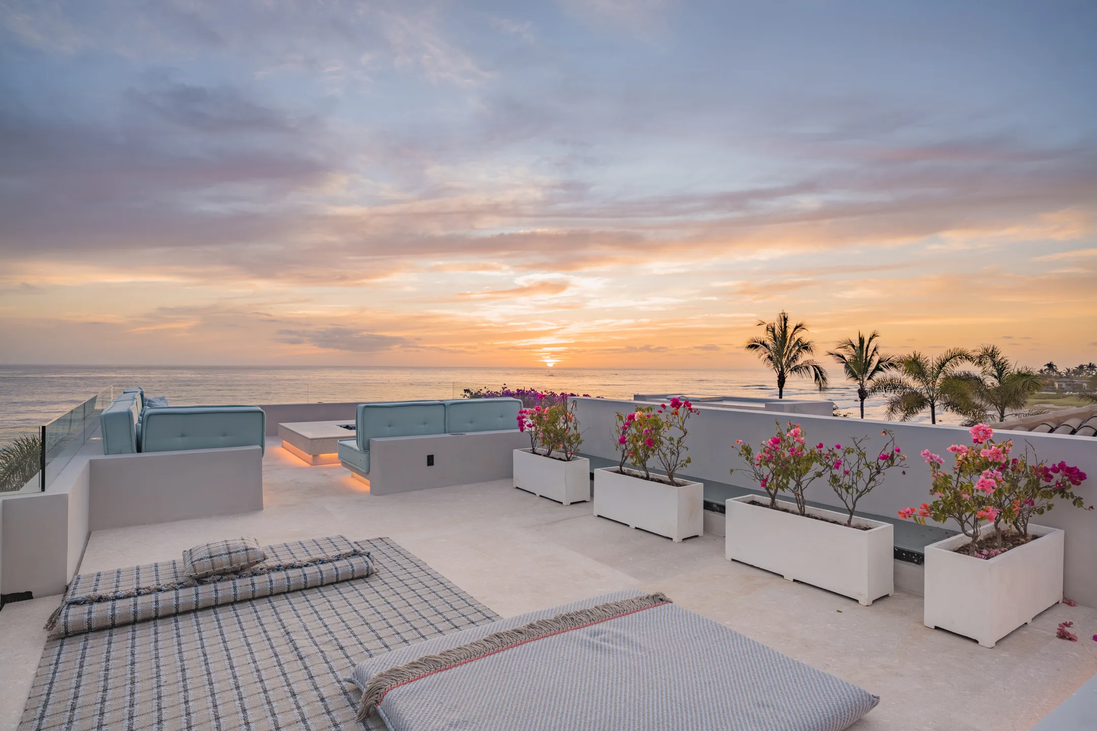 The sun setting into the Pacific from the rooftop lounge — daybeds and bougainvillea in the last light