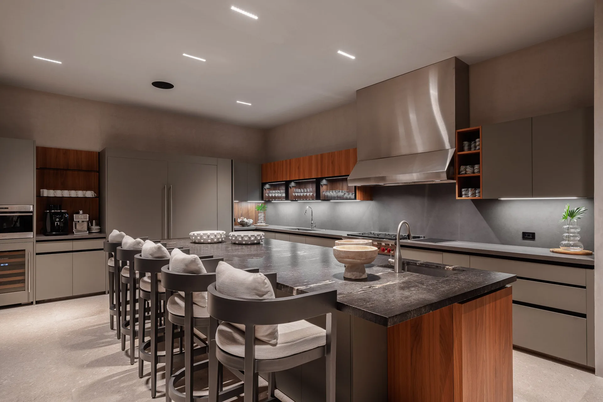 The show kitchen at night — the island glowing down its full length, stools along the run