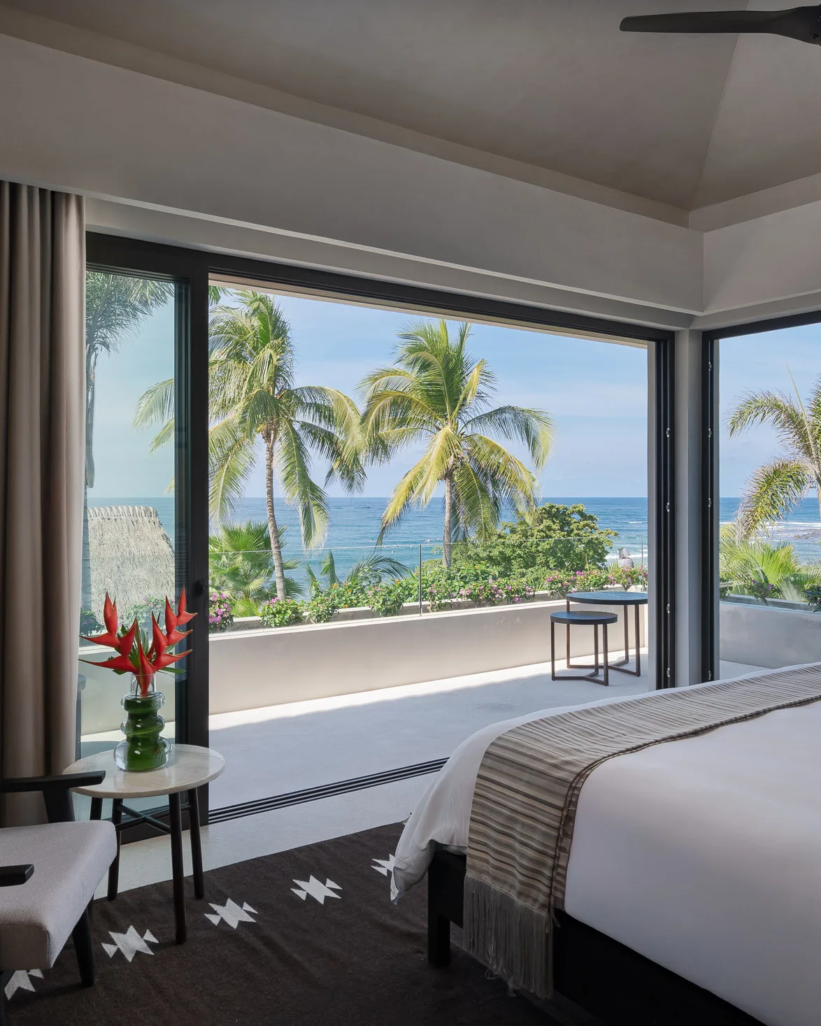 Skye — the bed facing wraparound corner windows, palms and ocean beyond