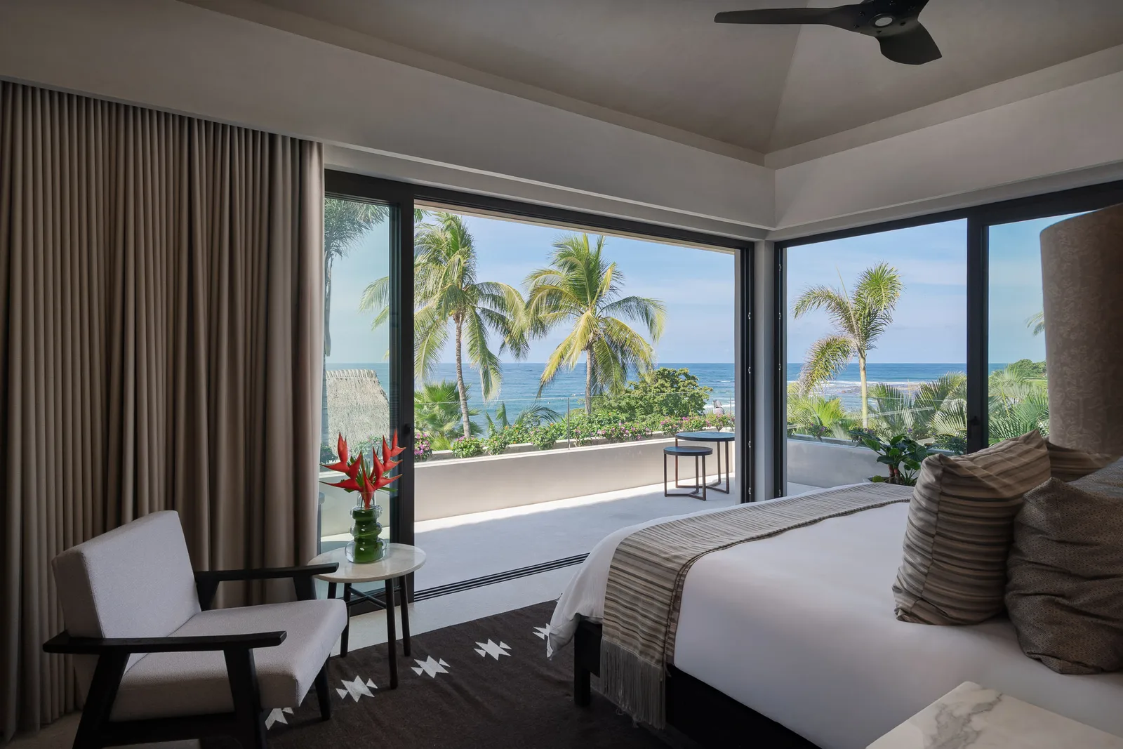 Skye — the bed facing wraparound corner windows, palms and ocean beyond