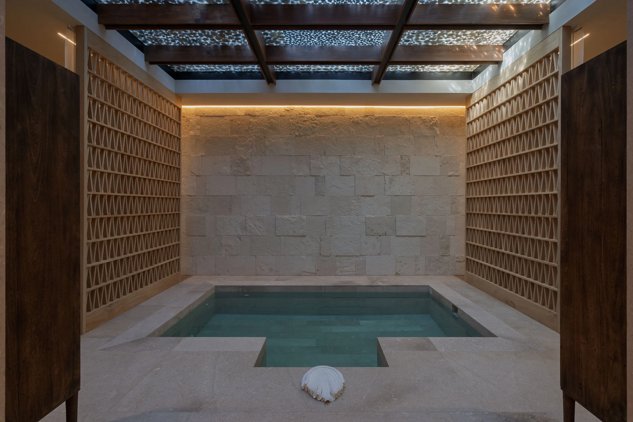 The spa’s cold plunge beneath a carved stone wall, lit in a warm glow