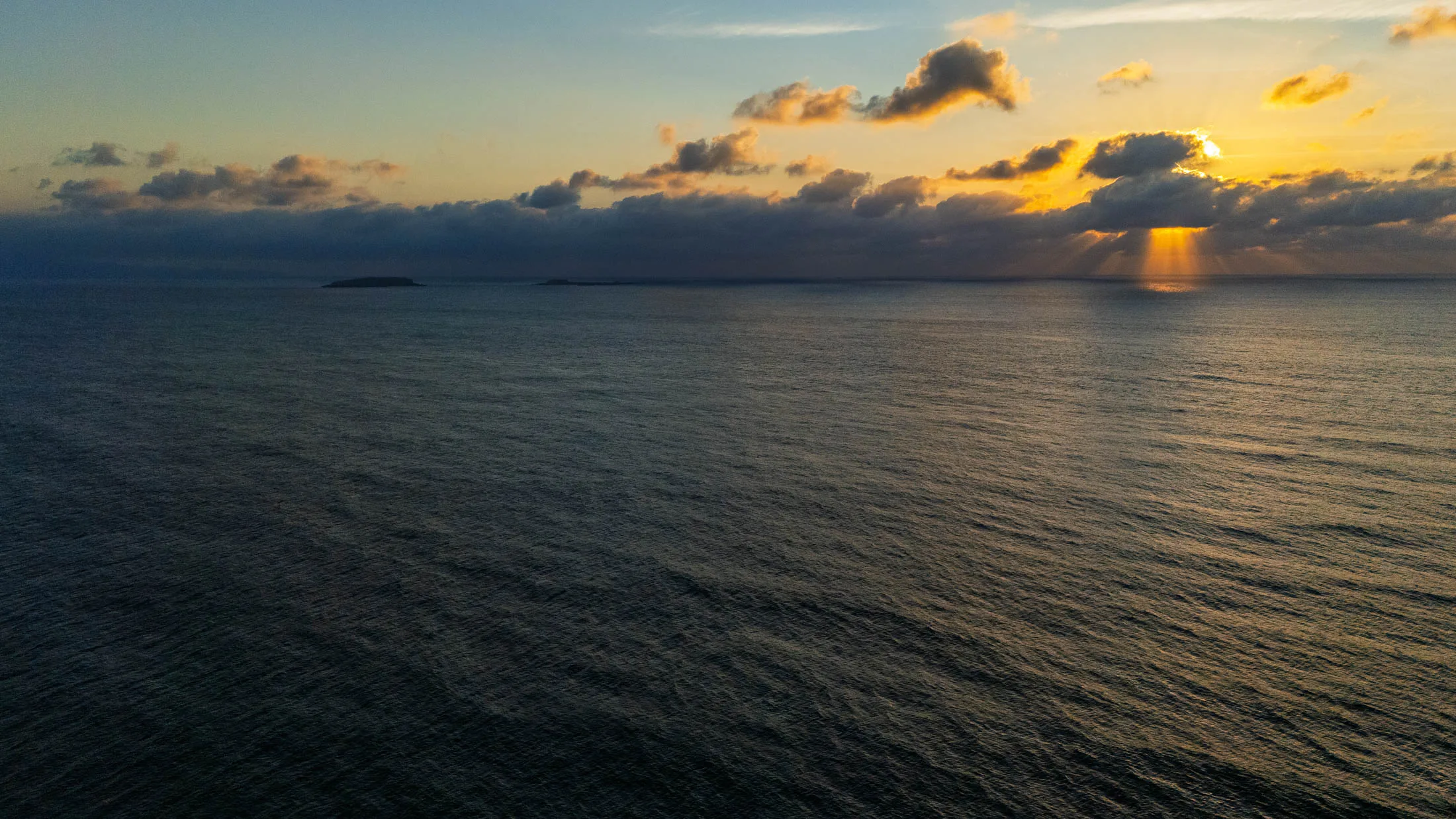 Sunset over the open Pacific off Punta Mita — the sun breaking through banked clouds, its light falling on calm water